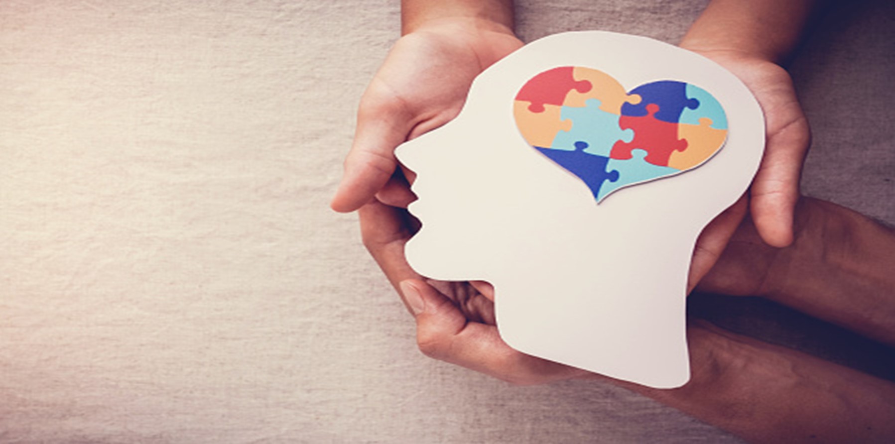 Hands holding a cardboard cut out of a persons face in profile with a heart shaped jigsaw where the brain would be.